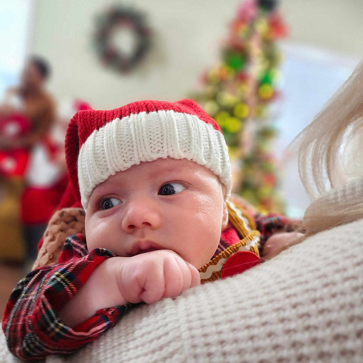 Henderson joined the competition — help win amazing prizes! baby, christmas_tree, closeup, cozy, curious, face, hand, hat, holding, holiday, indoor, infant, knit_hat, person, plaid_clothing, red, soft_focus, warm_clothing, white, wreath