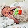baby, newborn, smiling, knitted_outfit, carrot_decoration, cushion, floral_pattern, cute, happy, infant, child, sleeping_area, cozy, hand, headwear, soft_texture, portrait, lying_down, indoors, warm