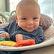 Kolter is registered to the contest to win money with this photo: baby, infant, smile, face, cushion, blanket, clothing, indoor, child, soft, cozy, cute, portrait, young, toddler, hand, blue_clothing, window, daylight, comfort