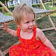 Chloé a rejoint le concours — aidez-le/la à gagner de superbes lots ! toddler, child, dress, orange, floral_pattern, outdoor, grass, deck_chair, leopard_print, wooden_frame, smiling, sitting, daylight, greenery, apartment_building, summer, playful, hair_clip, person, nature