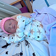 Dahlia is registered to the contest to win money with this photo: newborn, baby, sleeping, pajamas, pink_hat, star_pattern, blanket, butterfly_print, bed, adult_arm, resting, indoors, cozy, soft_lighting, child, infant, cute, peaceful, clothing, portrait