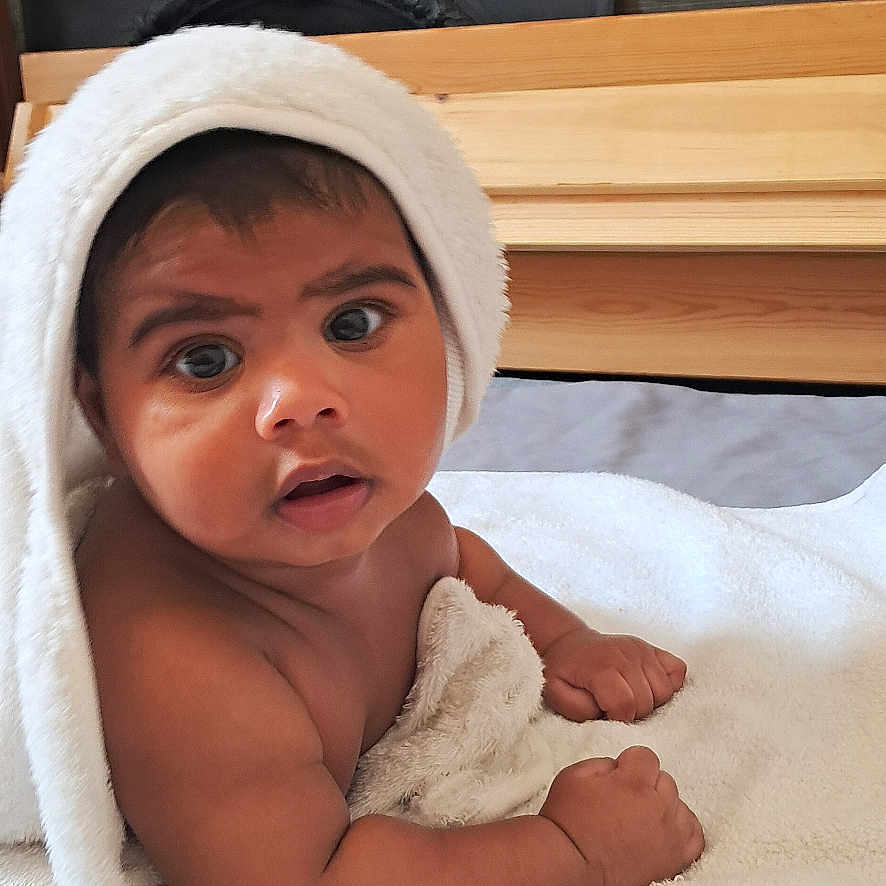 Revlon Fernandes is registered to the contest to win money with this photo: baby, bed, blanket, child, cozy, curious, cute, expression, eyes, face, hands, indoor, infant, portrait, skin, soft, texture, towel, warm, wood