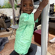 Malick a rejoint le concours — aidez-le/la à gagner de superbes lots ! child, toddler, smile, green_clothing, bracelet, platform, pole, outdoor, plants, chair, person, shoe, floor_tile, curtain, cage, adult, casual, happy, portrait, home