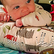 Tobias joined the competition — help win amazing prizes! baby, infant, pillow, animal_print, chewing, sleeve, indoor, adult, blurred_background, casual_clothing, face, head, hand, blue_eyes, patterned_fabric, colorful, resting, cute, child, person