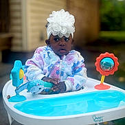 Jaior Milani is registered to the contest to win money with this photo: baby, baby_walker, background_blur, child, colorful_clothing, curious, expression, flower_headband, hands, headband, infant, jacket, outdoor, person, playful, seat, smile_absent, toddler, toy, young_child
