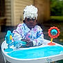 baby, baby_walker, background_blur, child, colorful_clothing, curious, expression, flower_headband, hands, headband, infant, jacket, outdoor, person, playful, seat, smile_absent, toddler, toy, young_child