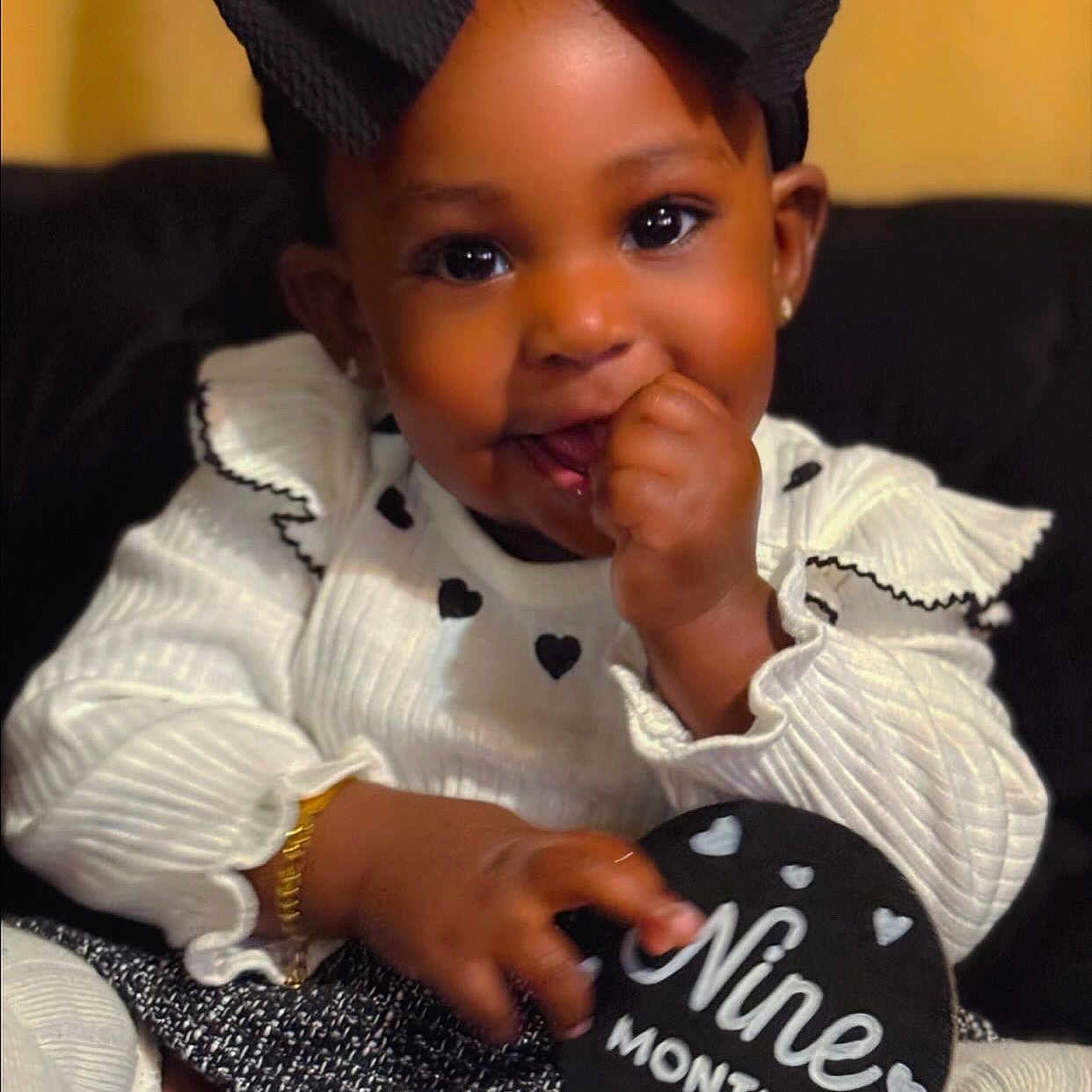 Jaior Milani is registered to the contest to win money with this photo: baby, black_bow, bracelet, celebration, child, couch, cute, fingers, girl, hand, happy, heart_pattern, indoor, infant, nine_months, portrait, sign, sitting, smiling, white_outfit