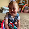 baby, child, smiling, bow, denim_overalls, white_shirt, carpet, fabric_book, colorful, indoor, toy, blurred_background, crawling, happy, person, infant, cute, playful, home, portrait