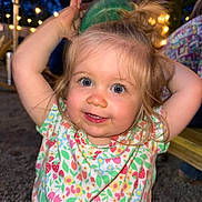 Lily is registered to the contest to win money with this photo: child, toddler, smiling, blue_eyes, blonde_hair, floral_shirt, outdoor, night, string_lights, playing, happy, cute, person, portrait, face, arm_raised, green_cup, hair_up, background_blur, fun