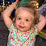 child, toddler, smiling, blue_eyes, blonde_hair, floral_shirt, outdoor, night, string_lights, playing, happy, cute, person, portrait, face, arm_raised, green_cup, hair_up, background_blur, fun