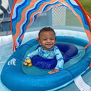 Jream is registered to the contest to win money with this photo: toddler, child, inflatable_pool, float, canopy, rubber_duck, water, swimming_pool, smiling, blue, outdoor, sunny, play, baby, summer, recreation, fun, toy, young_child, happy