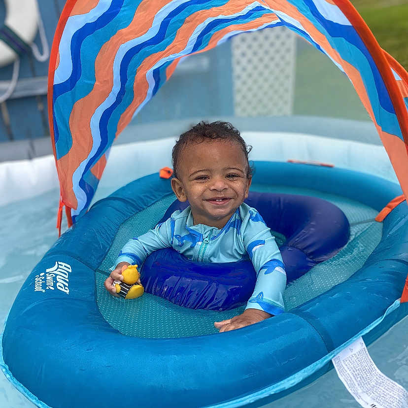 Jream is registered to the contest to win money with this photo: toddler, child, inflatable_pool, float, canopy, rubber_duck, water, swimming_pool, smiling, blue, outdoor, sunny, play, baby, summer, recreation, fun, toy, young_child, happy
