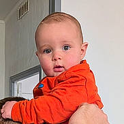 Bastien participe au concours pour gagner de l'argent avec cette photo : adult_hand, baby, bright_eyes, child, closeup, curious, cute, expression, face, hand, head, holding, indoor, infant, orange_clothing, person, portrait, skin, warm_clothing, young_child