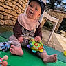 Bastien participe au concours pour gagner de l'argent avec cette photo : baby, background, cap, casual, child, clothing, daylight, foot, green_mat, happy, headwear, nature, outdoor, person, plastic_toy, playtime, sitting, smiling, stone_wall, toy