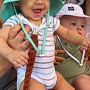 Valerian is registered to the contest to win money with this photo: baby, infant, child, hat, bucket_hat, smiling, curious, striped_onesie, green_onesie, adult_hand, toy, sitting, patterned_clothing, cute, indoor, person, footwear, sock, happy, holding