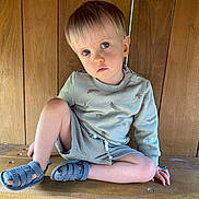 Elyott participe au concours pour gagner de l'argent avec cette photo : toddler, child, blue_eyes, sitting, wooden_bench, wooden_wall, casual_clothing, sweater, sandals, indoors, natural_light, portrait, cute, young_child, relaxed, bare_legs, hand_on_bench, serious_expression, short_hair, light_hair