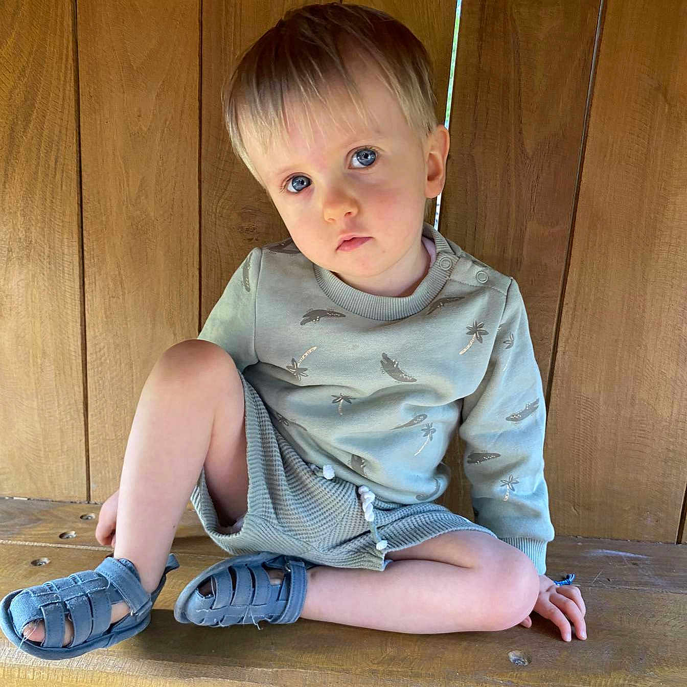 Elyott participe au concours pour gagner de l'argent avec cette photo : bare_legs, blue_eyes, casual_clothing, child, cute, hand_on_bench, indoors, light_hair, natural_light, portrait, relaxed, sandals, serious_expression, short_hair, sitting, sweater, toddler, wooden_bench, wooden_wall, young_child