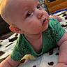 baby, infant, child, green_clothing, blanket, floor, indoor, furniture, face, skin, hand, curious, eyes, head, cute, toddler, home, soft_texture, carpet, room