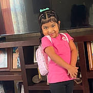 Camila joined the competition — help win amazing prizes! child, girl, smile, pink_shirt, black_shorts, backpack, indoor, furniture, television, photograph_frames, shoes, hair_bow, curtain, wooden_shelf, reflection, happy, portrait, standing, home, casual_clothing