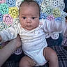 baby, infant, onesie, crocheted_blanket, pastel_colors, handmade, pattern, child, cute, face, skin, person, holding_hand, sitting, indoors, plush, soft, young_child, comfort, portrait