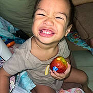 Toahei a rejoint le concours — aidez-le/la à gagner de superbes lots ! child, toddler, smile, apple, bite, happy, indoor, blanket, clothing, person, sitting, floor, toy, remote_control, diaper, furniture, face, hand, foot, home