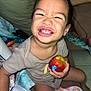 child, toddler, smile, apple, bite, happy, indoor, blanket, clothing, person, sitting, floor, toy, remote_control, diaper, furniture, face, hand, foot, home
