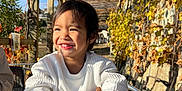 Toahei a rejoint le concours — aidez-le/la à gagner de superbes lots ! child, smiling, white_sweater, plastic_cup, outdoor, autumn, vines, wooden_pergola, sunlight, metal_table, happy, portrait, young_child, nature, daylight, casual_clothing, seated, table, plant, relaxed