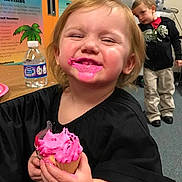 Zoey is registered to the contest to win money with this photo: child, toddler, cupcake, pink_frosting, smiling, messy, classroom, water_bottle, table, black_shirt, happy, indoor, person, young_child, playful, food, celebration, fun, background, curious