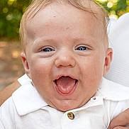 Dawson is registered to the contest to win money with this photo: baby, infant, smiling, happy, face, blue_eyes, white_shirt, buttons, portrait, closeup, child, person, outdoor, nature, background_blur, skin, expression, joy, hands, caucasian