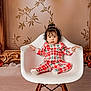 child, toddler, baby, chair, white_chair, plaid_pajamas, pajamas, holiday, christmas, ornaments, decorative_frame, portrait, studio, indoor, cozy, face, hair, sitting, cute, expression