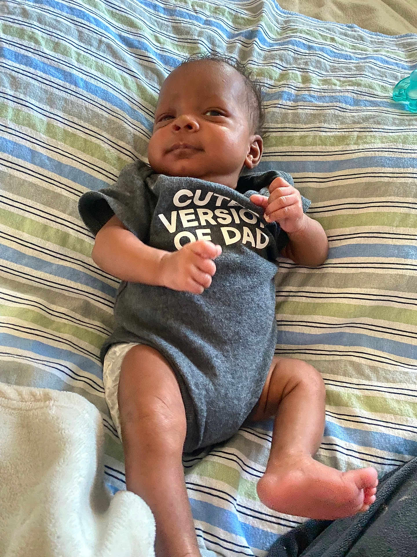 Semaj joined the competition — help win amazing prizes! baby, infant, onesie, clothing, striped_bedspread, lying_down, cute, expression, fist, skin, foot, hand, bed, blanket, child, person, indoor, newborn, smile, portrait