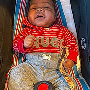 Semaj is registered to the contest to win money with this photo: baby, child, infant, car_seat, red_hoodie, striped_clothing, gray_pants, blanket, seatbelt, smiling, happy, indoor, person, cute, portrait, clothing, toddler, comfort, holding, strap