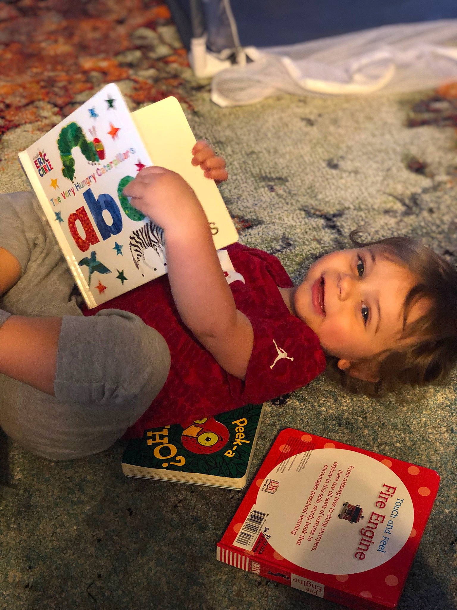 Kannon is registered to the contest to win money with this photo: baby_toddler_clothing, book, carmine, child, flooring, font, fun, grass, happy, human_leg, joy, nail, pattern, person, play, sitting, smile, t_shirt, thigh, toddler
