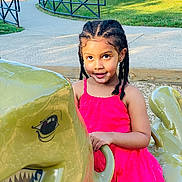 Eureka is registered to the contest to win money with this photo: child, girl, braided_hair, pink_dress, playground, dinosaur_ride, outdoor, daylight, park, play_equipment, smiling, happy, person, fence, sidewalk, grass, trees, sunlight, holding, recreation