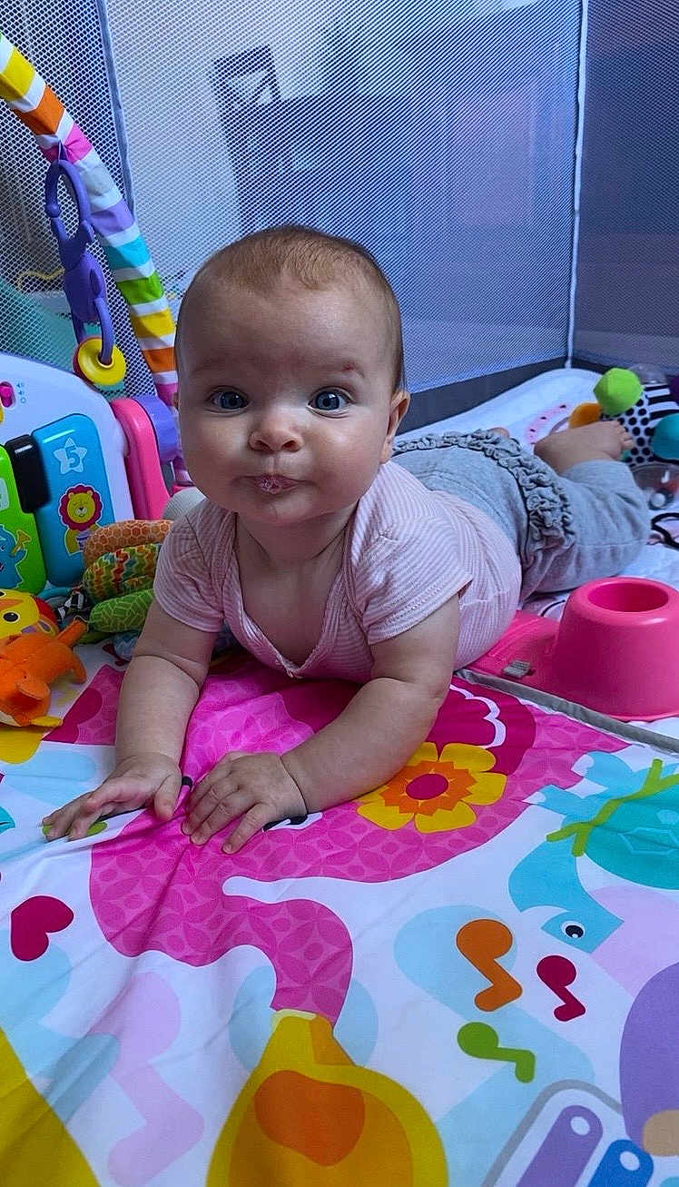 Talia joined the competition — help win amazing prizes! baby, infant, play_mat, toys, colorful, onesie, tummy_time, activity_center, plush_toy, mesh_side, floor, portrait, blue_eyes, chubby_cheeks, hands, crawling_pose, curious, indoor, playpen, rattle