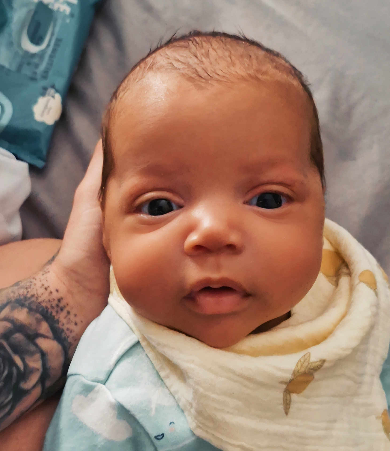 Tavontae is registered to the contest to win money with this photo: baby, infant, face, close_up, hand, tattoo, bib, clothing, blue, expression, eyes, skin, newborn, cute, portrait, person, soft, indoor, cozy, child