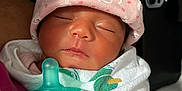 Adeline joined the competition — help win amazing prizes! newborn, baby, sleeping, pacifier, pink_hat, blanket, patterned_background, face, infant, cute, peaceful, wrapped, child, indoors, person, closeup, soft_lighting, resting, cozy, tiny