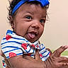 baby, child, face, tongue, headband, blue_bow, curly_hair, earrings, striped_shirt, strawberry_pattern, hand, holding, smile, playful, indoor, person, cute, portrait, infant, skin