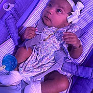 Khalani is registered to the contest to win money with this photo: baby, infant, child, headband, bow, floral_dress, white_socks, baby_carrier, straps, pacifier, purple_light, cute, gazing, curious, indoors, soft_lighting, closeup, portrait, comfort, resting