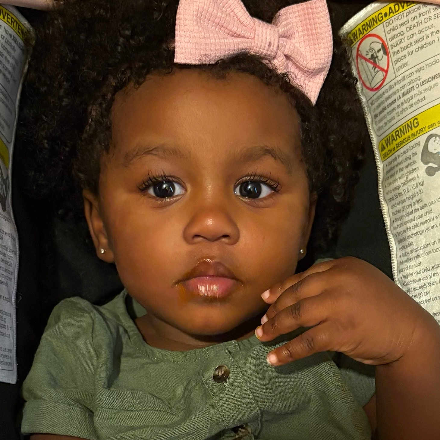 Samani is registered to the contest to win money with this photo: baby, car_seat, child, closeup, clothing, curly_hair, cute, earrings, expression, eyes, face, food_stain, green_shirt, hand, indoor, person, pink_bow, portrait, skin, toddler