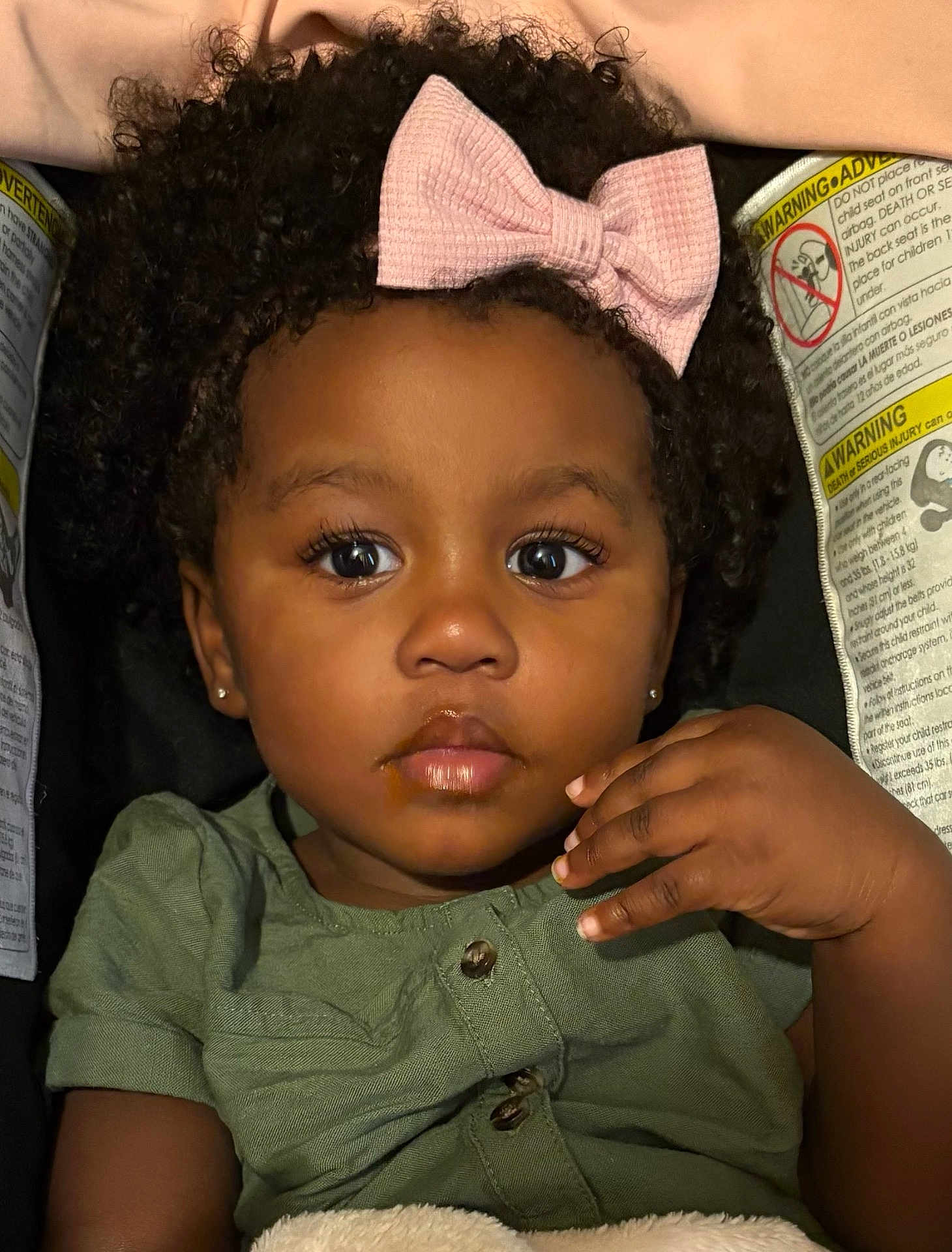 Samani is registered to the contest to win money with this photo: toddler, child, face, curly_hair, pink_bow, green_shirt, car_seat, eyes, hand, food_stain, portrait, indoor, cute, baby, skin, expression, person, clothing, earrings, closeup