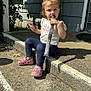 Tessa is registered to the contest to win money with this photo: casual_clothing, chewing, child, concrete_step, daytime, girl, greenery, house, navy_leggings, object, outdoor, pink_bows, pink_crocs, portrait, shadow, sitting, sunlight, toddler, wall, white_shirt