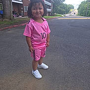 Sophia joined the competition — help win amazing prizes! child, curly_hair, pink_outfit, shorts, sneakers, smile, outdoor, road, tree, building, grass, sidewalk, suburban, number_10, happy, person, casual_clothing, daylight, playful, young