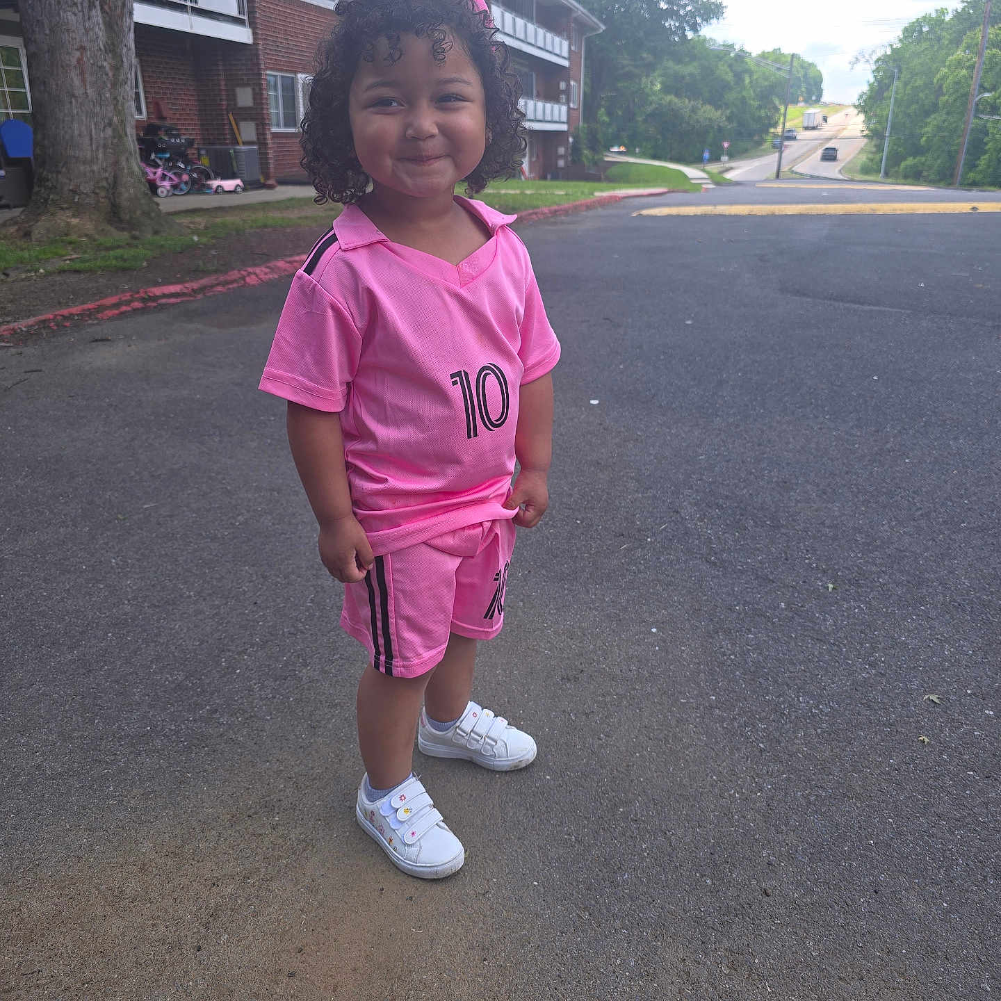Sophia joined the competition — help win amazing prizes! building, casual_clothing, child, curly_hair, daylight, grass, happy, number_10, outdoor, person, pink_outfit, playful, road, shorts, sidewalk, smile, sneakers, suburban, tree, young