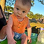 baby, child, outdoor, sunlight, orange_clothing, blue_shorts, table, hand, face, person, nature, tree, grass, daylight, bottle, can, summer, curious, expression, park