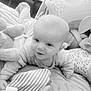 baby, infant, plush_toy, soft_toy, bed, blanket, pillow, smile, face, person, child, indoors, cute, lying_down, comfort, cozy, monochrome, striped_toy, happy, toddler
