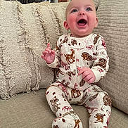 Juni joined the competition — help win amazing prizes! baby, child, infant, smiling, pajamas, animal_print, couch, pillows, indoor, happy, cute, sitting, clothing, furniture, home, cozy, portrait, face, hands, expression