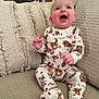 baby, child, infant, smiling, pajamas, animal_print, couch, pillows, indoor, happy, cute, sitting, clothing, furniture, home, cozy, portrait, face, hands, expression