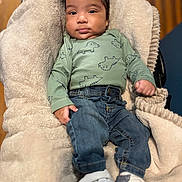 Yeshua is registered to the contest to win money with this photo: baby, child, infant, blanket, clothing, jeans, sneakers, dinosaur_pattern, face, person, indoor, cute, soft_texture, relaxed, young, footwear, sitting, casual, portrait, cozy