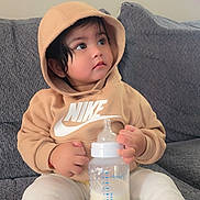 Sizda is registered to the contest to win money with this photo: toddler, child, hoodie, nike, milk_bottle, milk, sitting, couch, grey_couch, indoors, curious, clothing, baby, person, casual, cozy, soft_lighting, portrait, young_child, comfortable